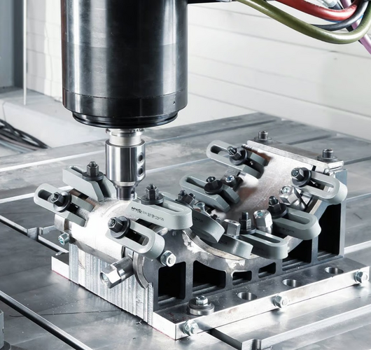 Nahaufnahme einer CNC-Fräsmaschine, die ein metallisches Werkstück auf einem Spannvorrichtungs-Tisch bearbeitet; gut sichtbar sind Frässpindel, Spannklauen und die präzise ausgerichtete Werkstückaufnahme.