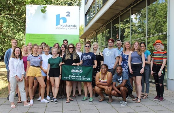 Group photo of young adults in front of a building at Magdeburg-Stendal University of Applied Sciences; some are holding a banner from the University of South Carolina Upstate.