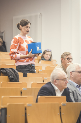 A participant speaks from the audience in a lecture theatre.