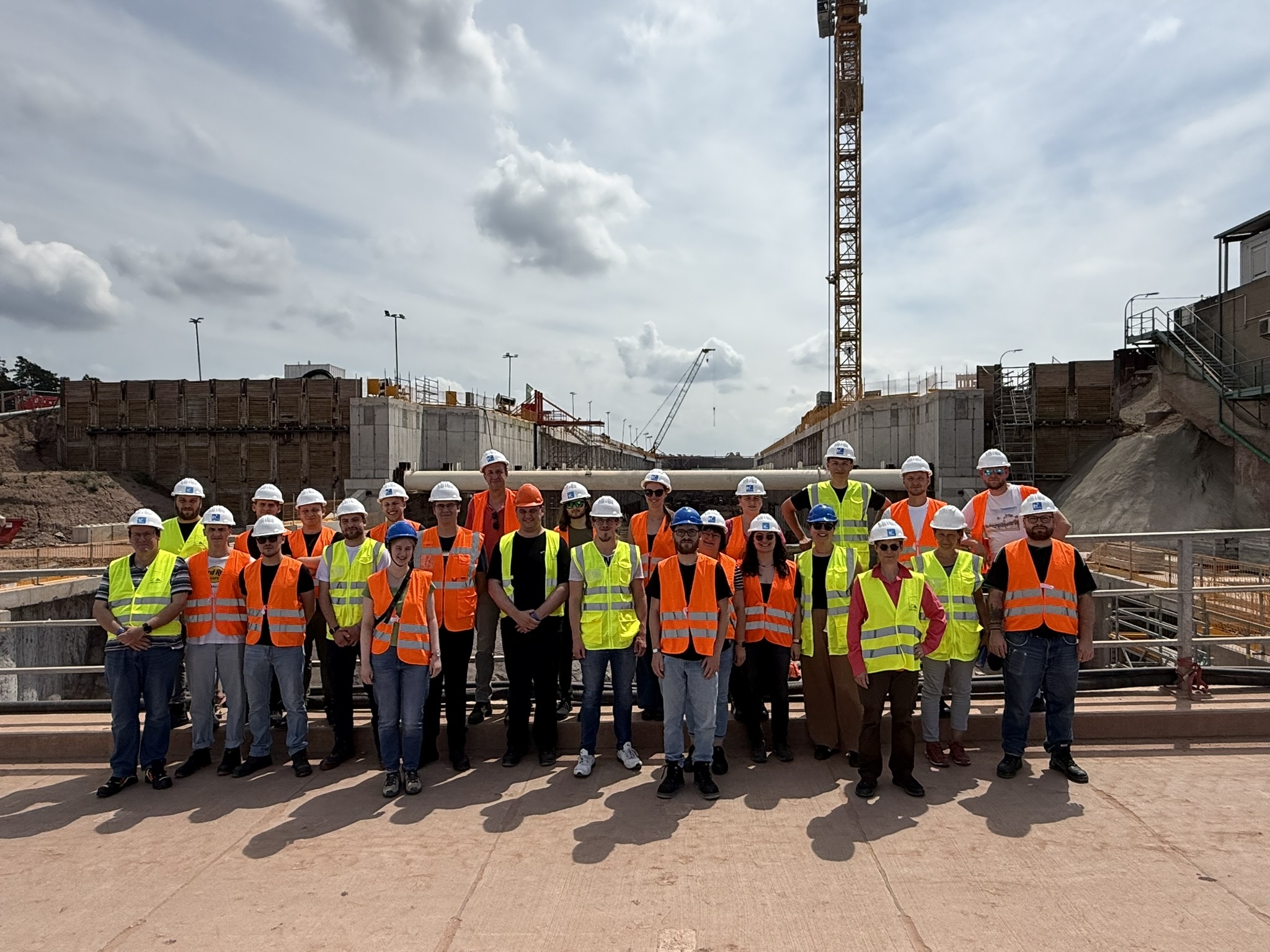 Gruppenfoto aller teilnehmenden Studierenden und Mitarbeitenden vor der Baustelle des Neubaus der Schläuse in Kriegenbrunn. Sie alle tragen eine Warnweste.
