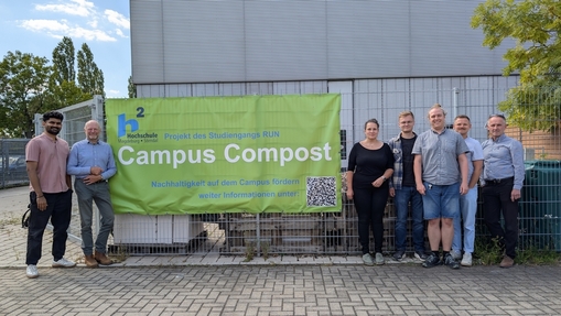 Die Mitglieder der Arbeitsgruppe stehen auf dem Campus an einem grünen Plakat mit dem Projektnamen Campus Compost