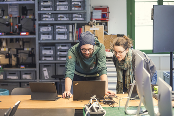 The image shows two people in the X-Lab makerspace looking at a laptop together.