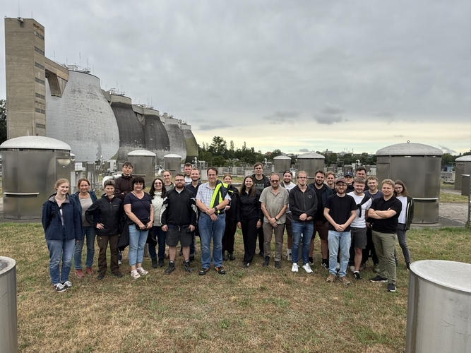 Group photo of the participating students and staff at the Muggenhof Wastewater Treatment Plant in Nuremberg, taken in front of the plant's anaerobic digesters.