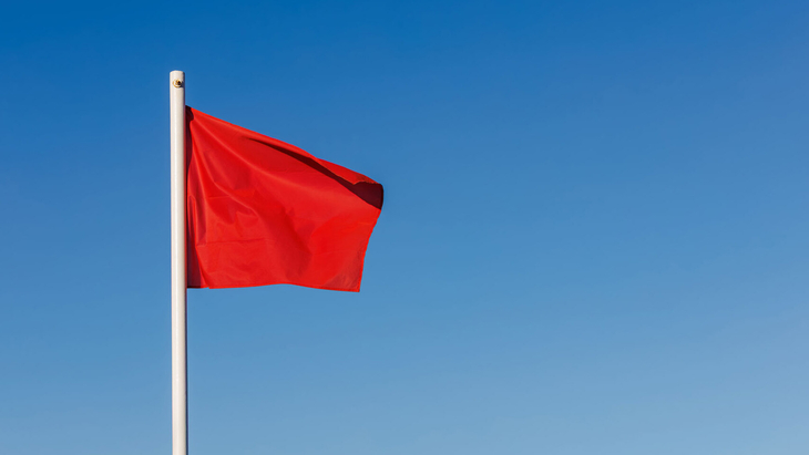 Eine rote Fahne weht an einem Mast vor blauem Himmel.