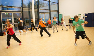 Studierende üben Hip-Hop-Tanzschritte in der Bewegungshalle ein.