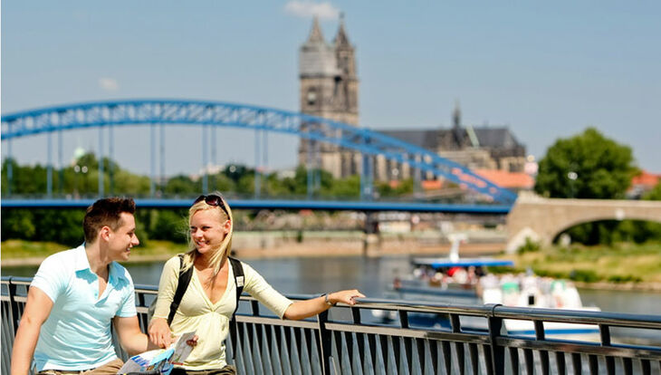 Zwei junge Radfahrer stehen am Magdeburger Elbufer und schauen in einer Radkahrte nach dem Weg, im Hintergrund sind Elbe, Sternbrücke und Magdeburger Dom zu sehen