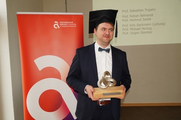 A doctoral graduate from Hochschule Anhalt proudly holding an award after successfully defending his dissertation