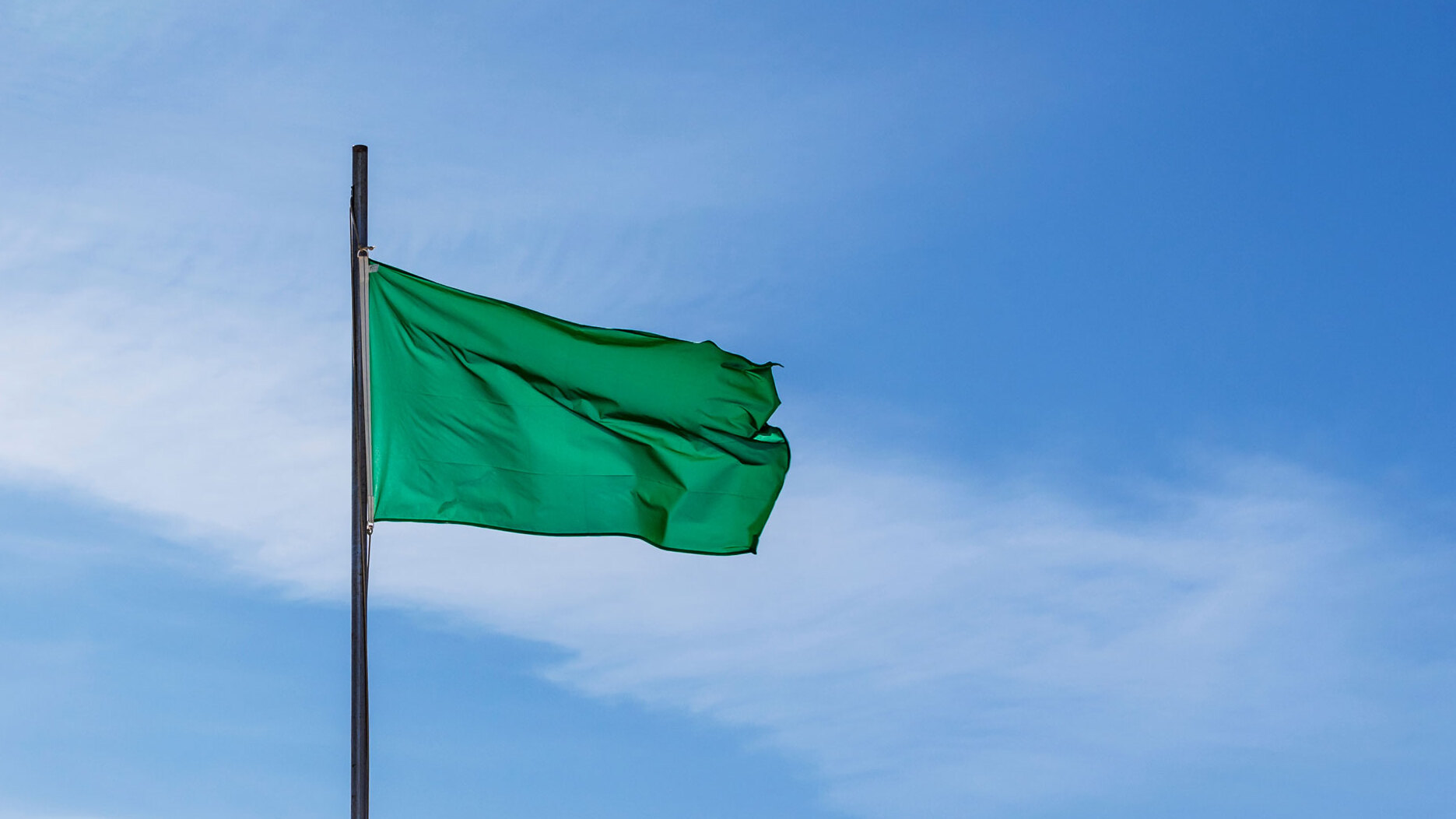 Eine grüne Fahne weht an einem Mast vor blauem Himmel mit leichten Wolken.