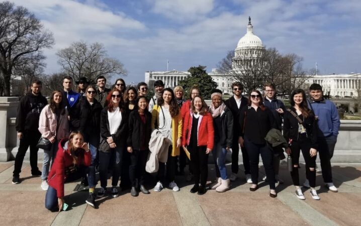 A group of young people pose in front of the Capitol in Washington, D.C. in sunny weather.