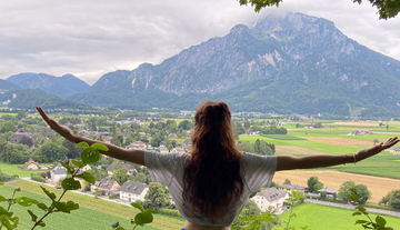 Frau mit ausgebreiteten Armen vor einer Bergkulisse