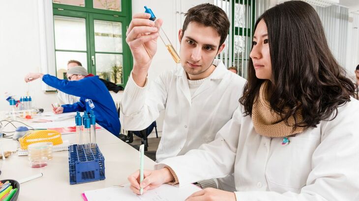 Zwei Studierende in Laborkitteln untersuchen eine Flüssigkeitsprobe