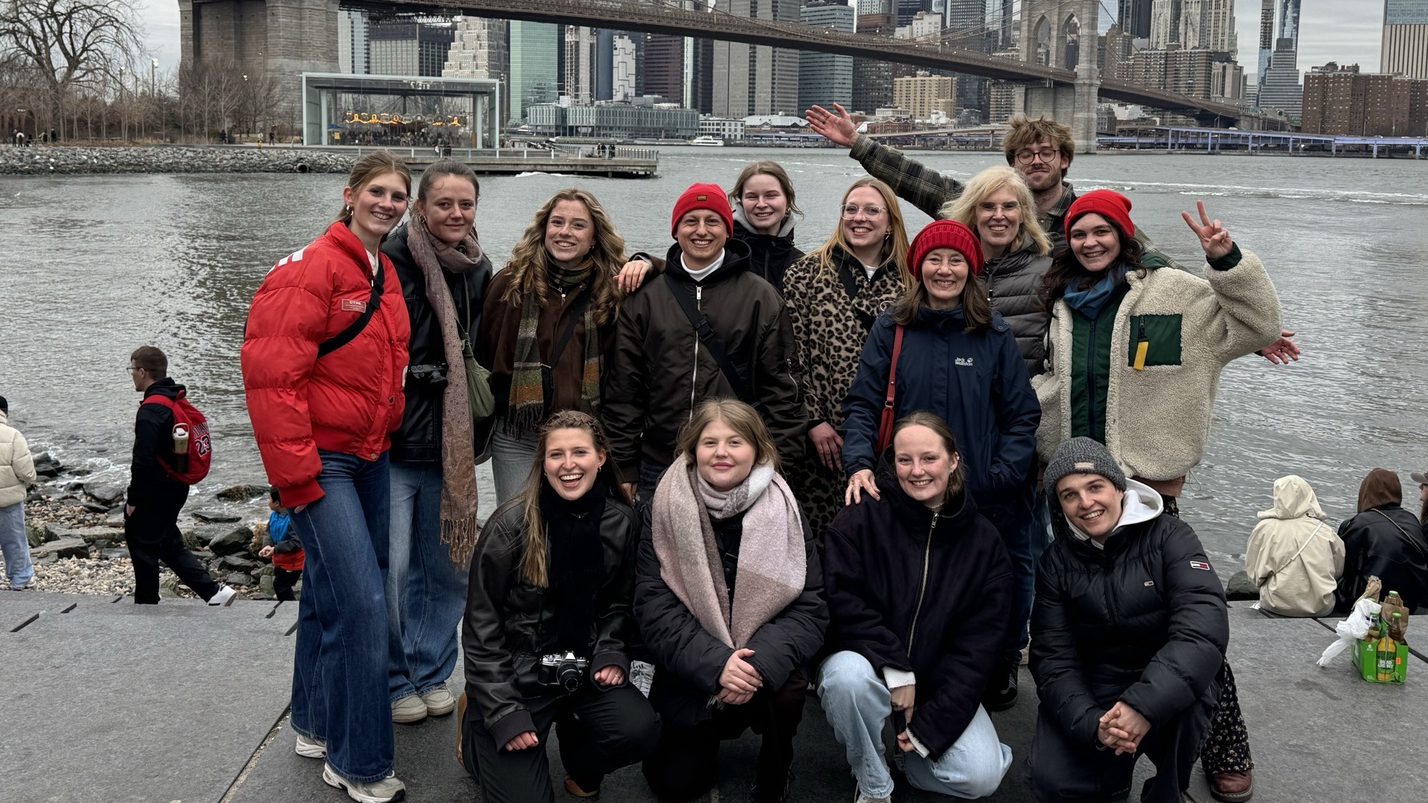 Eine Gruppe von Menschen posiert am Ufer vor der Brooklyn Bridge und der Skyline von New York.