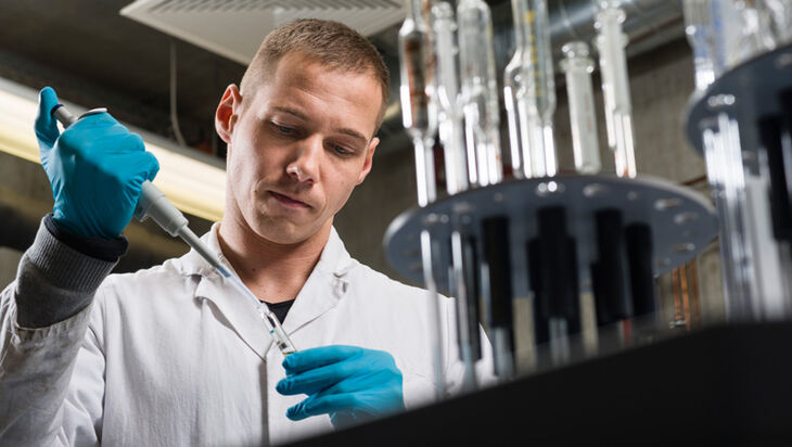 Ein mit Laborkittel und Handschuhen bekleideter Mitarbeiter pipettiert im Labor eine Flüssigkeit
