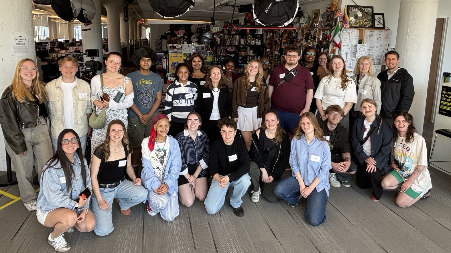 Eine große Gruppe von Studierenden oder Teilnehmenden posiert in einem Raum mit professioneller Beleuchtung und vielen Postern an der Rückwand.