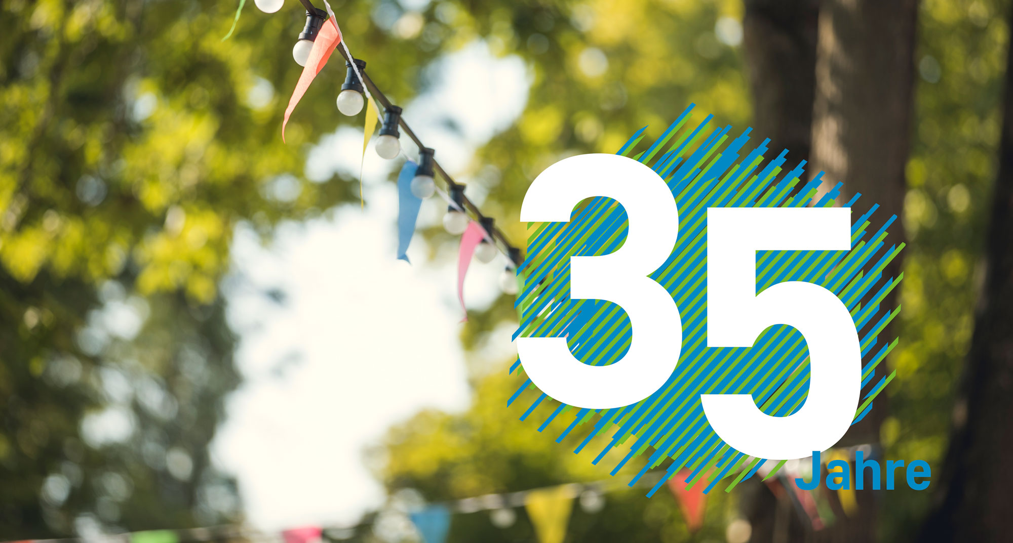 Großer Schriftzug „35 Jahre“ vor unscharfem grünen Hintergrund mit festlicher Girlanden- und Lichterkette