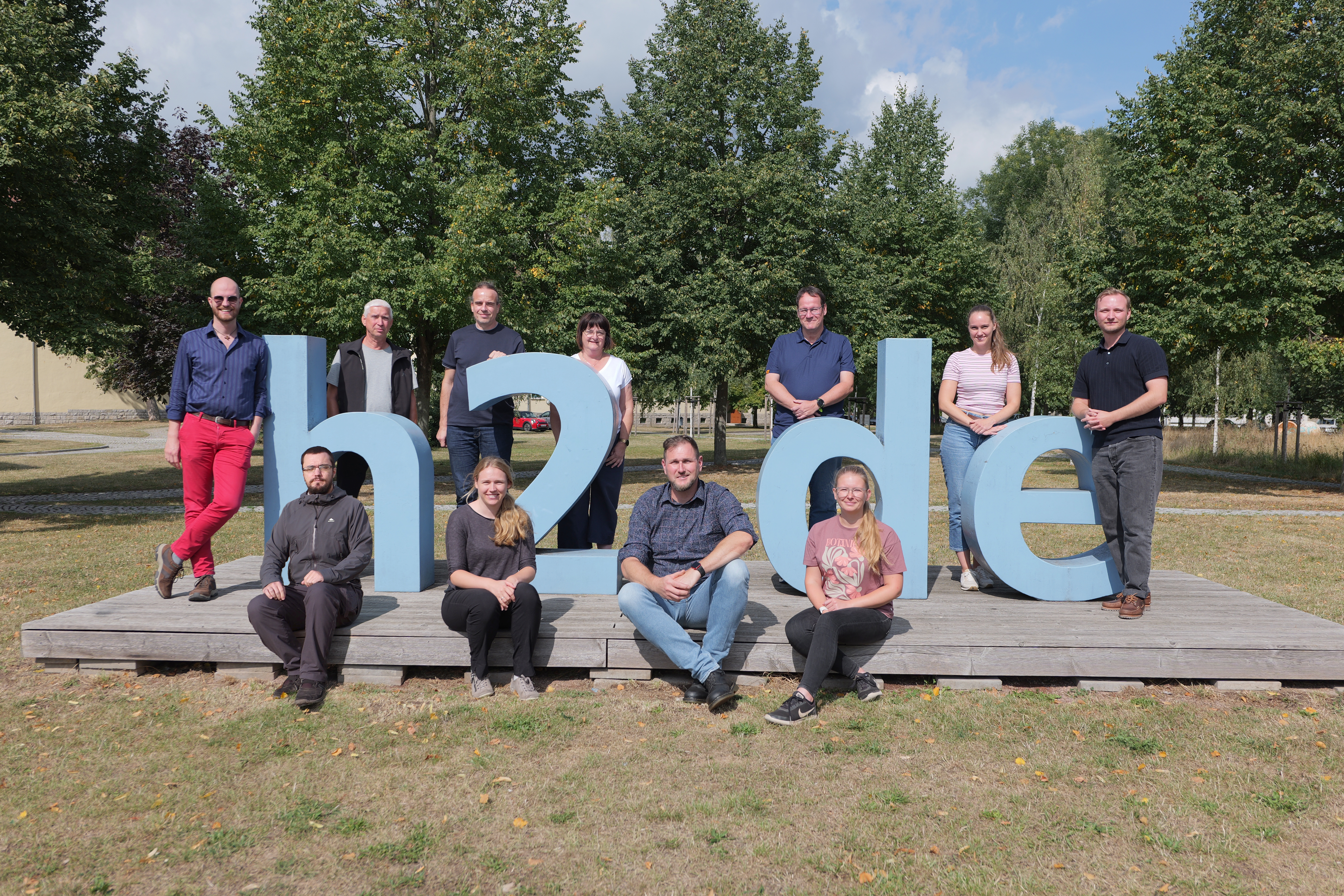 Gruppenfoto aller Angestellten aus der Abwassergruppe draußen vor und um das H2-Logo drum herum.