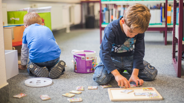 Zwei Jungen spielen in der Bibliothek auf dem Fußboden mit einem Puzzle.
