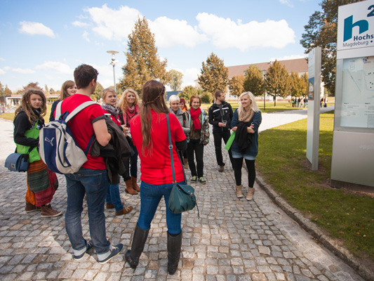 Studentische Mentoren in roten Shirts erklären neue Studierenden den Lageplan des Campus
