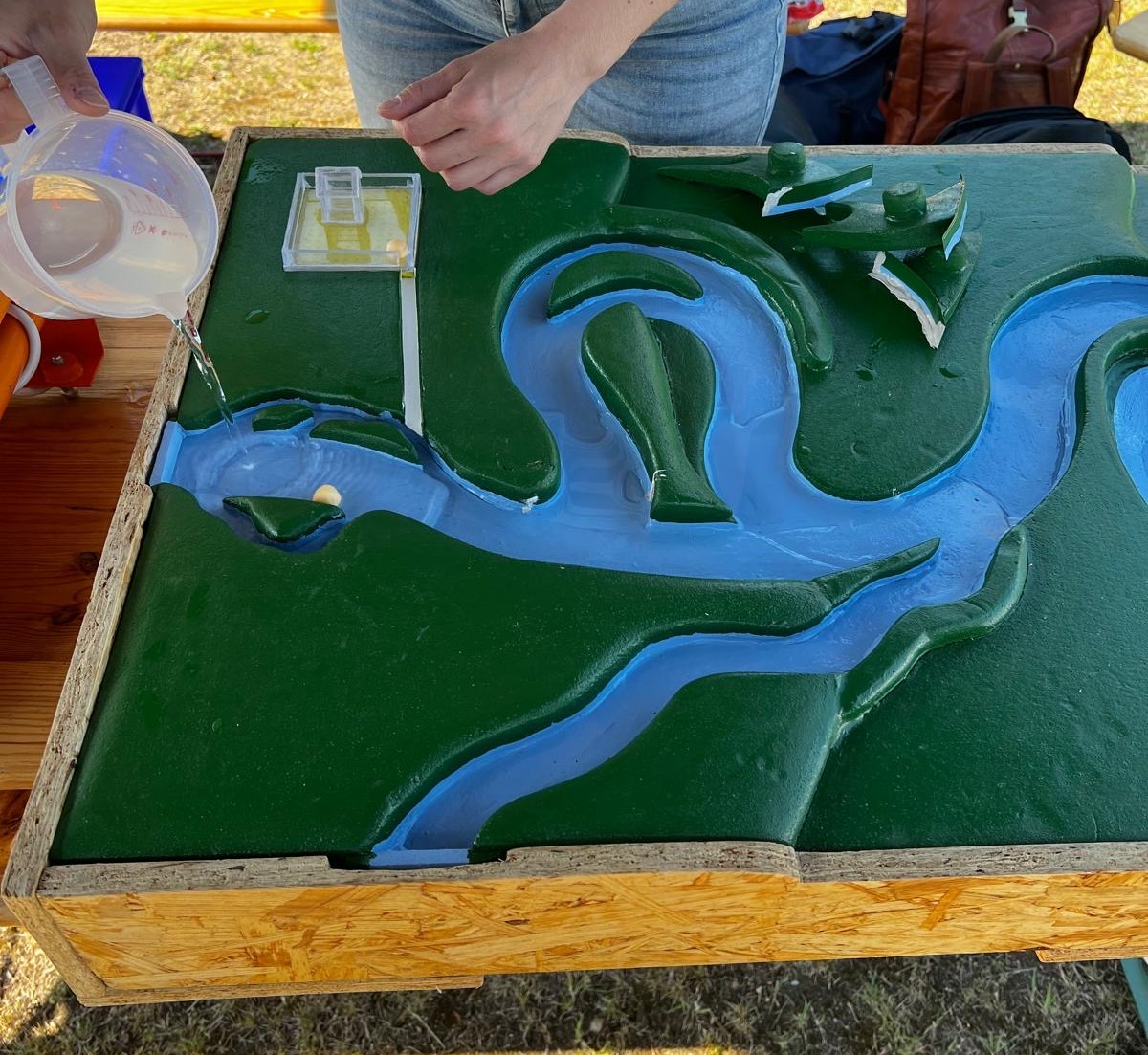 Experimenteller Aufbau eines Landschaftmodelles, anhand dessen den Kindern veranschaulicht wird, welchen Einfluss das Eingreifen des Menschen auf die Flussform hat und welchen Folgen das nach sich zieht, als auch welchen Einfluss die Versiegelung von Städten und Landschaften auf das Ökosystem Fluss und das leben der menschen in der stadt hat in Bezug auf Hochwassergefahren.